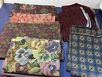 Photo showing assorted folded upholstery and tapestry fabrics with floral and geometric patterns.