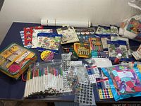 Photos show a collection of assorted kids craft supplies spread out on a table including markers, pens, stickers, fabric paint, glue, ribbons, trims, sponges, and stencils.
