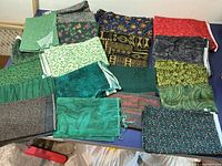 Multiple folded fabric pieces on table showing variety of colors and prints including florals, abstracts, and solids