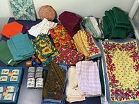 Wide top-down view of various cloth napkins, placemats, napkin rings, and other table linens including solid and floral patterns and small containers.