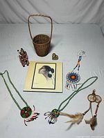 Overview of all items in the lot including the ceramic tile, woven basket, figurine, magnet, and beaded necklaces