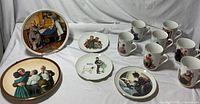 Collection of Norman Rockwell plates and mugs displayed on white fabric background.