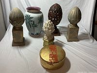 Front view of all items including the large ceramic palm tree vase, decorative finials in gold-tone, white sculpted, rust metal, and the gold box in front.