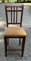 Front view of single wooden barstool showing upholstered seat and grid pattern backrest.