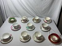 Photo showing 11 vintage bone china teacups and saucers in various floral patterns, colors and designs on a white tablecloth.
