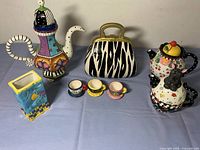 Wide shot of all items in the lot showing teapots, cookie jar, and cups arranged on a blue cloth.