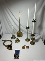 Full view of all brass items on white table including candle holders, bed warmer, horn, decorative brass pieces, and vintage watch gear.