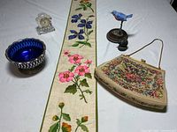 Overview of lot showing needlepoint wall hanging, needlepoint purse, blue glass bowl with silver base, Waterford Crystal clock, and two bird figurines.
