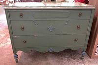 Front view of green painted dresser with three drawers, brass lion ring pulls, blue accents, mosaic top under glass, paint chipping visible