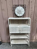 Full view of white vintage wicker shelf with wall art piece mounted above. Shows general shape and overall condition of the shelf and art.
