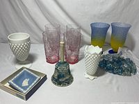 Full lot overview showing pink glass cups, Wedgewood dish in box, maritime bell, milk glass vases, gradient blue/yellow vases, and blue glass beads.