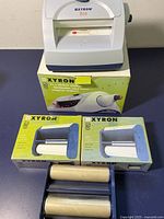 Xyron 510 craft machine on top of original box with two unopened cartridge boxes and two opened cartridges lying in front.