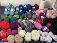Wide view of the yarn lot showing a large assortment of colors and textures including blue, green, purple, gray, beige, black, white, and multicolor speckled yarn.