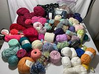 Full lot of yarn skeins displayed on a table, showing a large variety of colors and types including sparkly and fringy yarns