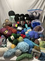 Wide top-down photo showing varied colored yarn skeins spread on surface, predominantly black and blue with some green, brown, and red.