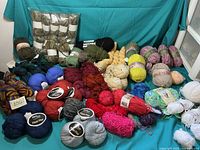 Wide assortment of yarn skeins arranged on teal fabric showing different colors and textures including green, brown, blue and pink hues.