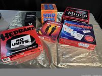 Photo showing six board game boxes including HeadBanz No Limits, MadGab, CodeNames, Dirty Minds, Rummikub Classic, and a black box game.