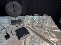 Photo showing the Bose speaker, six brandy snifters, and black circular sculpture arranged on a table.