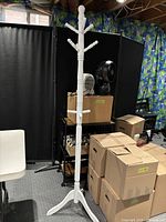 Full view of the white wooden coat tree standing among boxes and furniture in a room with dark curtains.