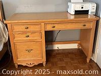 Front view of the blonde wooden desk showing four drawers - three smaller and one larger lower drawer.