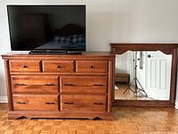 Front view of wooden low boy dresser with seven drawers and detached mirror positioned to the right.