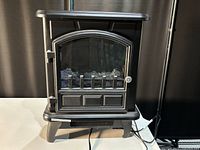 Close-up front view of the black electric fireplace showing its compact size, door, and faux log interior.