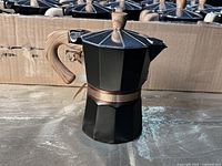 Close-up of a 6 inch tall espresso maker showing black body, metallic lid with wood-tone knob and handle.