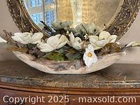 Faux floral decorative centerpiece in a curved wood bowl with white and pale green flowers and green foliage.