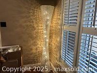 Full view of the tall glass floor lamp illuminated, showing its sparkling crystal design and the light pattern on the wall.