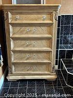 Front view of tall, light colored wood dresser with five drawers and glass pulls, showing the full height and wood grain