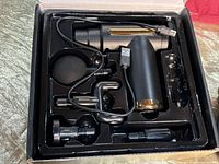 Massager in original black and gold packaging with several interchangeable massage heads and a USB charging cable.