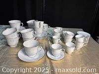 Full view of the ten coffee cups with saucers and ten espresso cups with saucers arranged on a blue cloth.