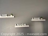 Three white floating shelves mounted on gray wall, each with large white letters spelling 'Live', 'Laugh', and 'Love'. Two shelves also have small white pots with green fake plants.