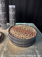 Stack of 10 small and 16 large leopard print plates with black edges on a table.