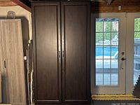 Full view of the tall chocolate brown portable pantry cabinet in a room next to a glass door, showing its external appearance and context.