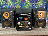 Photo of Philips portable stereo main unit flanked by two speakers with orange and black design, placed on wooden surface.