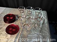All items shown together including 8 red glass plates stacked, 3 clear glass wine goblets and 4 clear martini glasses with red decoration on a cloth surface