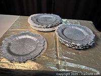 Set of silver-colored chargers stacked in three piles on a gold textured surface, clearly showing scalloped edges and textured wood grain pattern