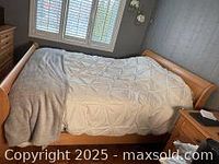 View of the blonde wood low profile sleigh bed with bedding in a bedroom setting, showing headboard and footboard shape and design.