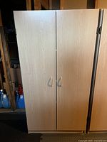Closed view of one light wood storage cupboard with two doors and metal handles.