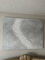 Photo of canvas print featuring a textured swoosh design in greys and whites on a neutral wall, showing full piece and texture details.