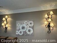 Two black wall sconces mounted on the wall, each with 5 lit lights and cream fabric shades, showing the decorative style and size relative to wall and ceiling.