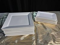 Stack of white square plates showing flat center and raised rim, set on a reflective surface.