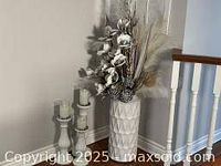 Photo of tall white ceramic vase with floral arrangement beside a staircase, showing full height and pattern of vase with flowers.