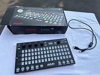 Akai Fire MIDI controller with USB cable and original box on white background.