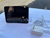 Front angled view of the Amazon Echo Show smart display and power adapter placed on white cloth, screen off