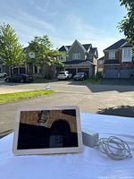 Amazon Echo Show displayed outside on white cloth with power adapter connected. Shows device front with screen and camera at top.