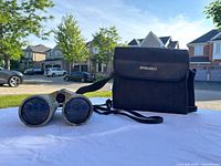 Binoculars and carrying case outdoors on white fabric surface under sunlight