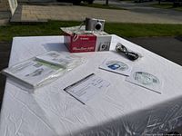 Canon PowerShot A85 camera, original box, manuals, cables, software CDs displayed on table outdoors