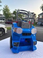 Front view of the blue and gray plastic front part of child's ride-on car showing headlights, grille and roll bar